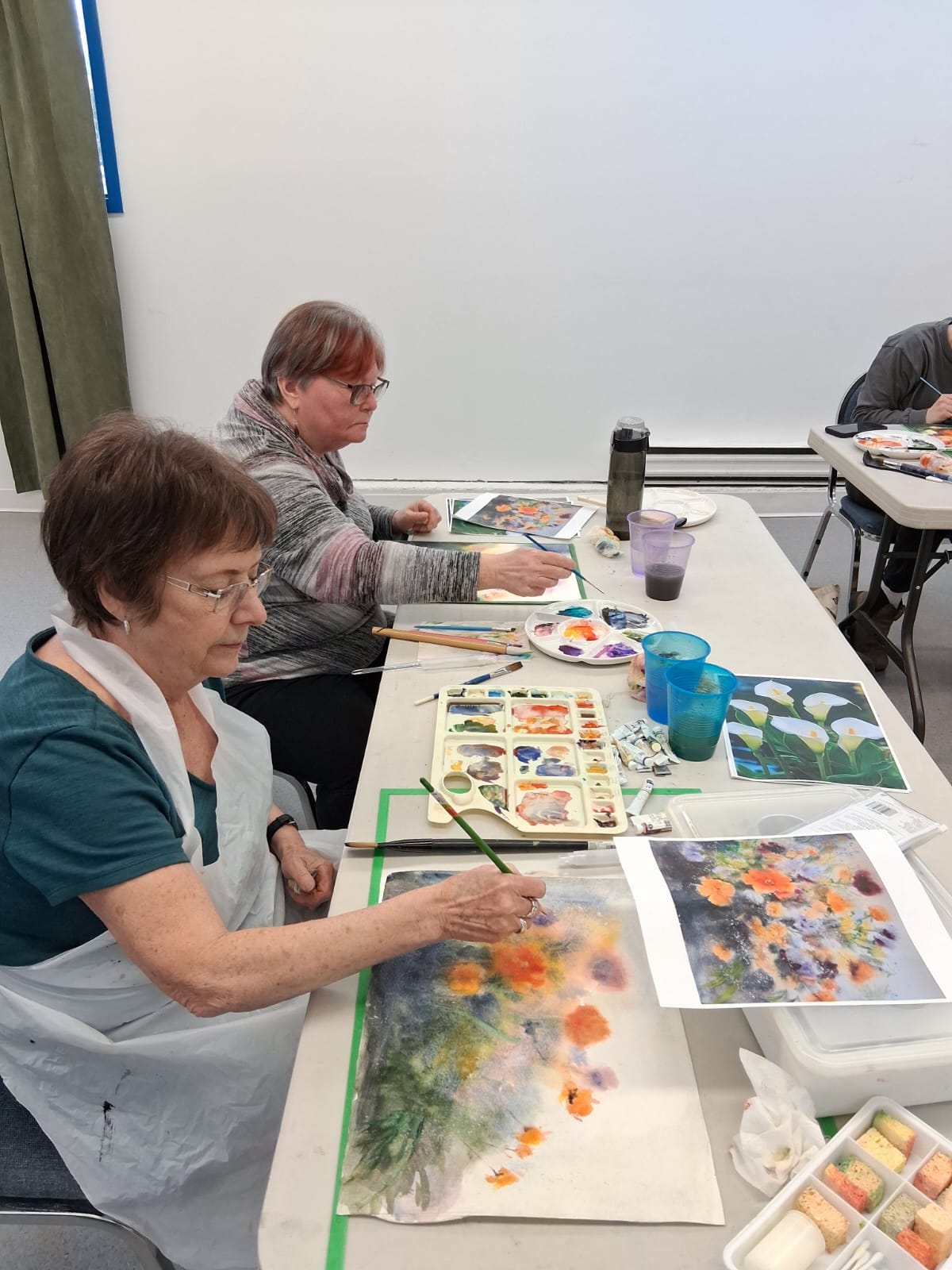 Workshop students painting floral watercolour studies from reference photos at a shared table, palettes and brushes in hand during one of Coral Ye Chen's watercolour workshops.